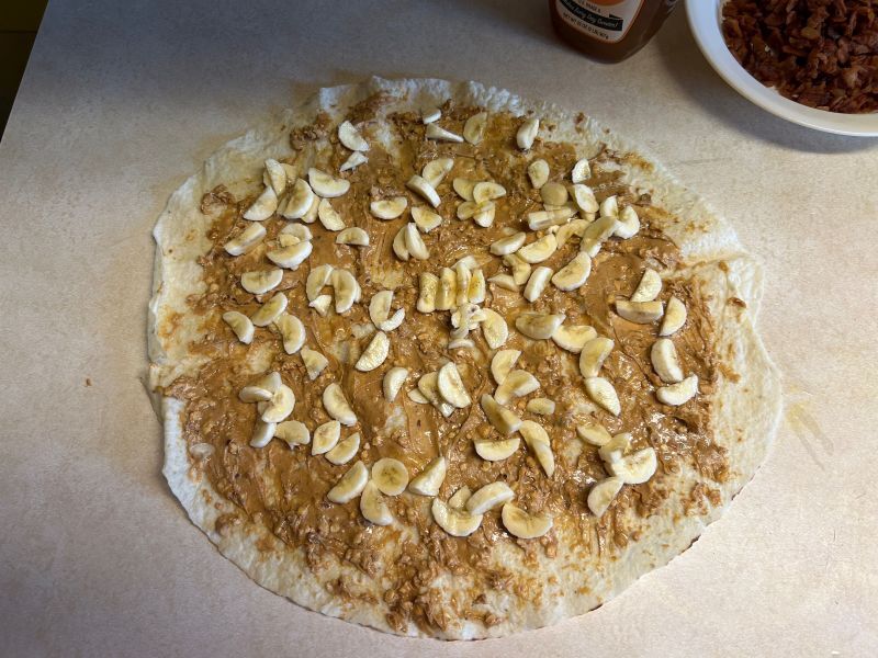 Spreading peanut butter and sliced bananas on a round of lefse