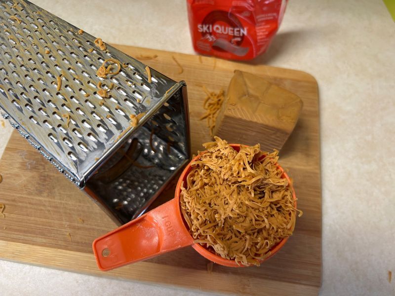Finely grated Gjetost cheese on cutting board for bread