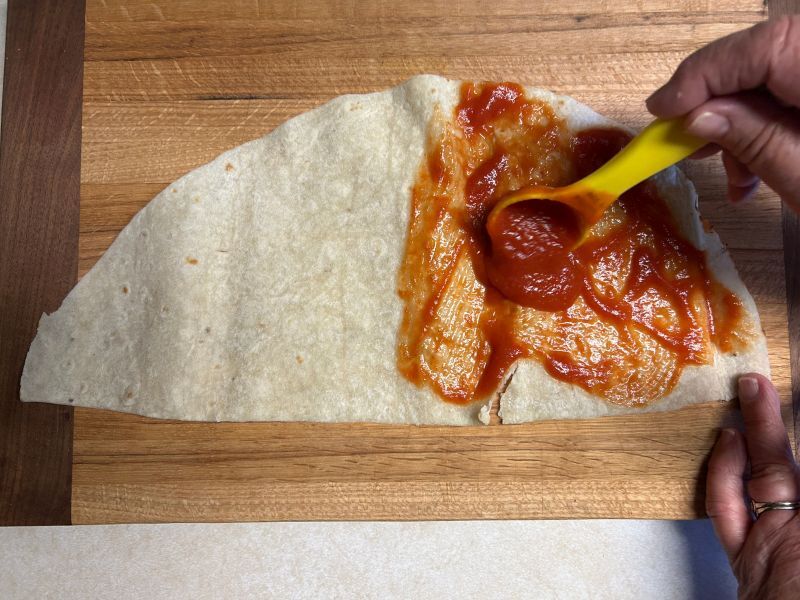 Spreading marinara sauce on a half-quarter of lefse