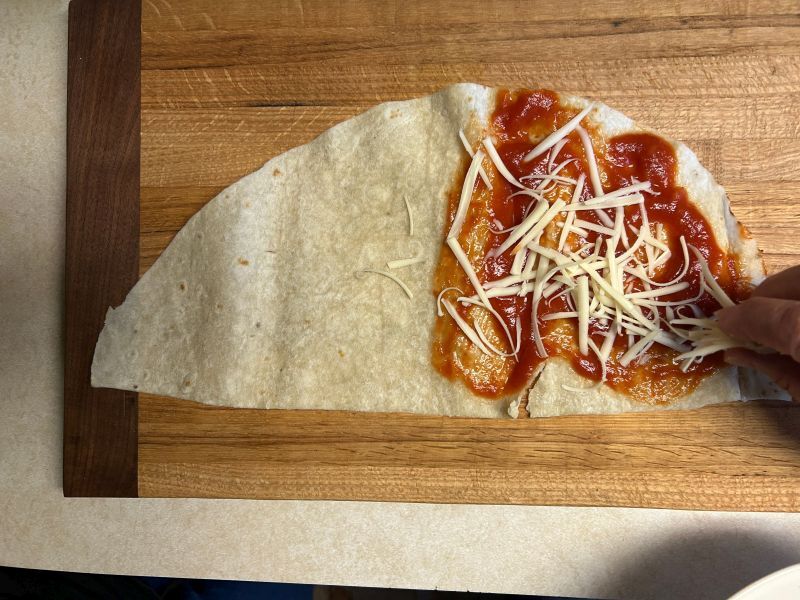 Adding shredded mozzarella on top of the sauce