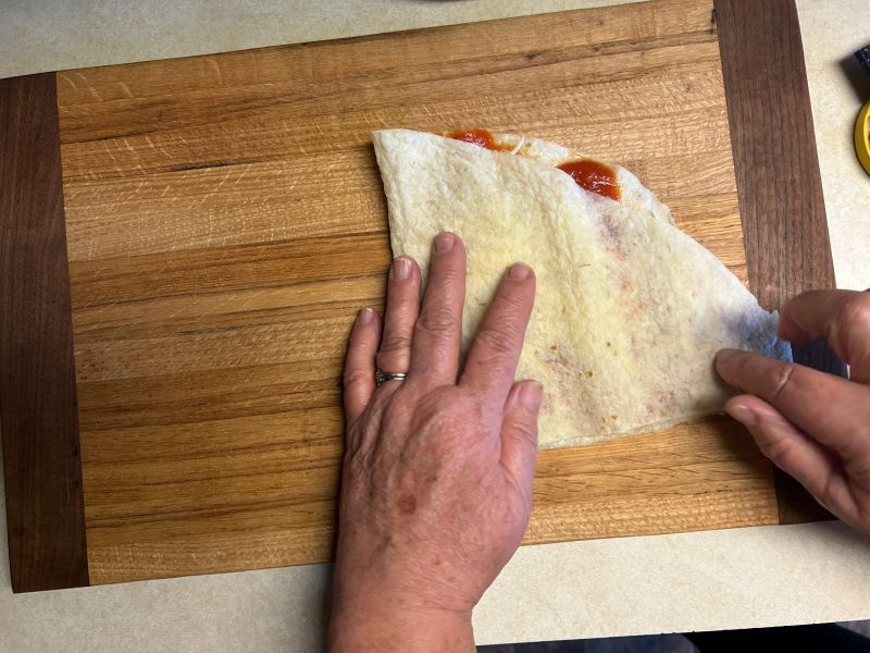 Folding lefse quarter over sauce and cheese