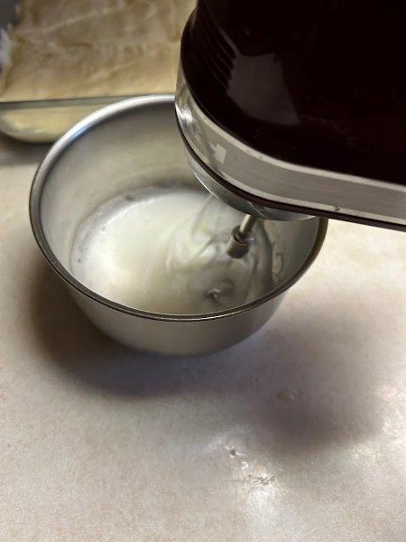 Egg white beaten to foam is ready to add over the top layer of crescent roll dough.