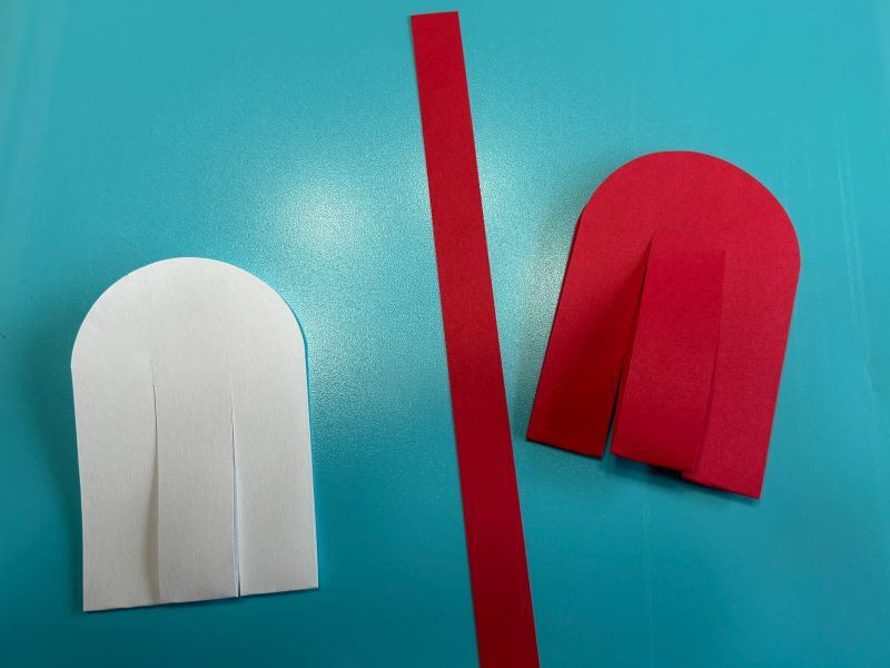 Red and white paper rectangles cut, folded, and prepared for weaving Scandinavian heart baskets.