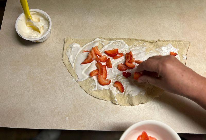 Adding fresh strawberries on top of yogurt-covered lefse